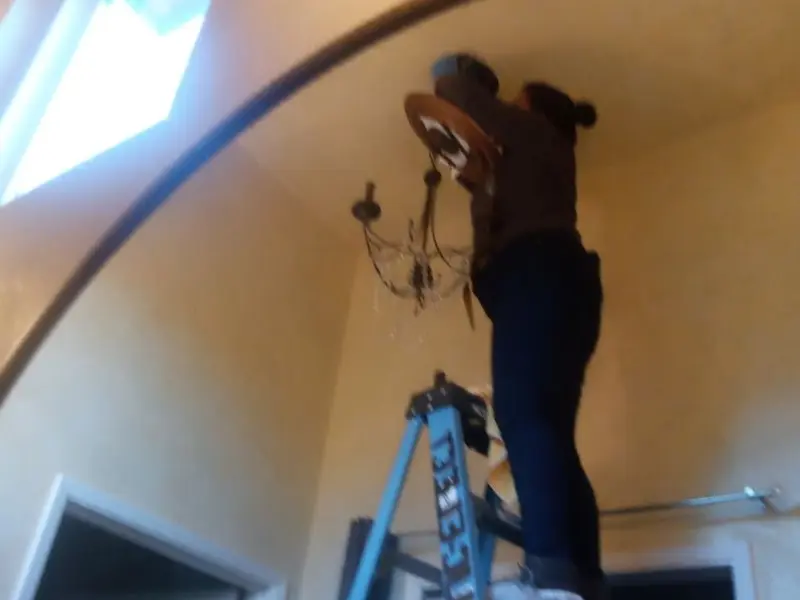 Electrician installing a chandelier in a Avenue B and C residence